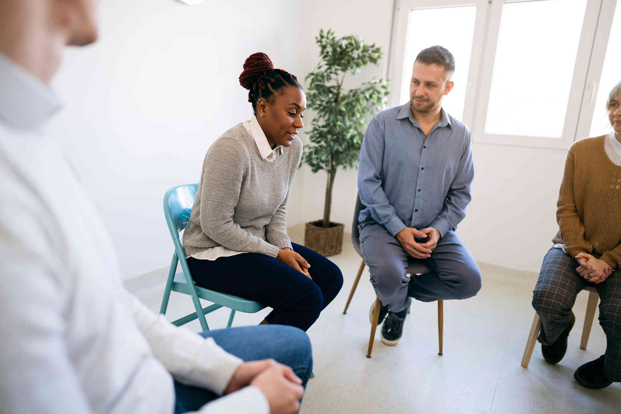 A group of woman sit in a circle during group therapy as a woman in a grey sweater talks.